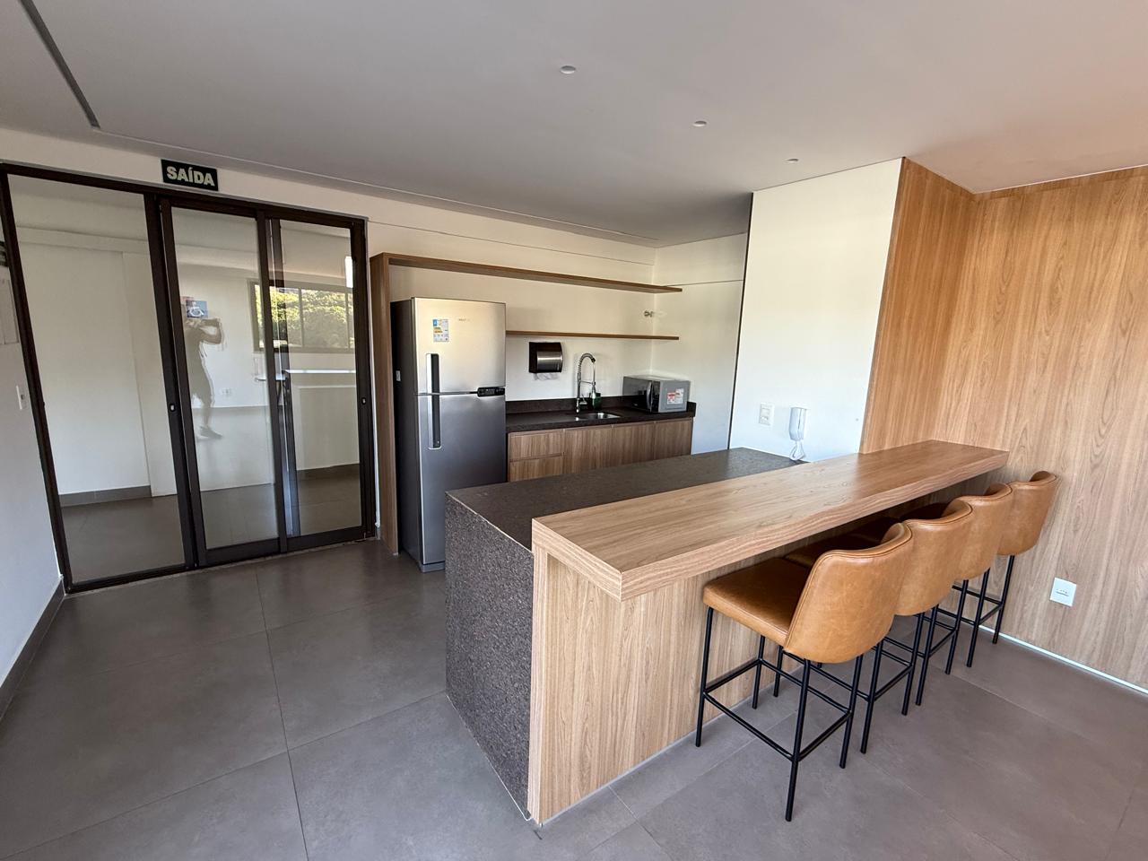 Espaço gourmet com bancada em granito, banquetas e cozinha de apoio
