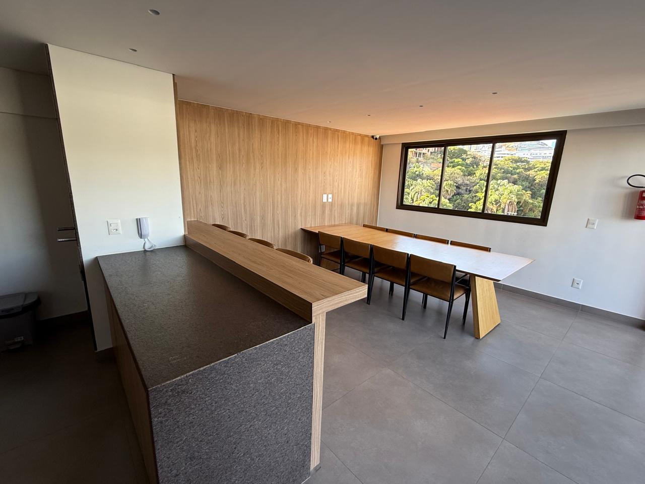 Salão de festas com mesa comunitária e vista para a área verde