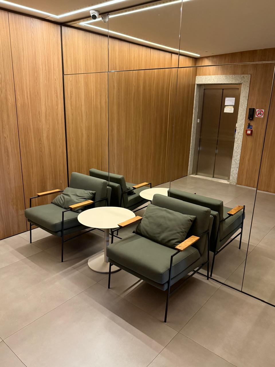 Hall de entrada com marcenaria em madeira, poltronas verdes e elevador