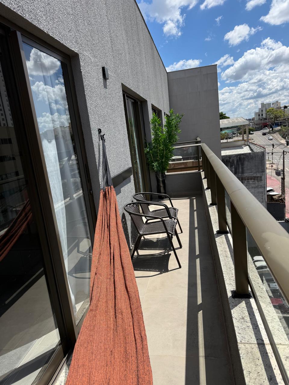 Varanda do apartamento com rede de descanso, poltronas e vista da cidade