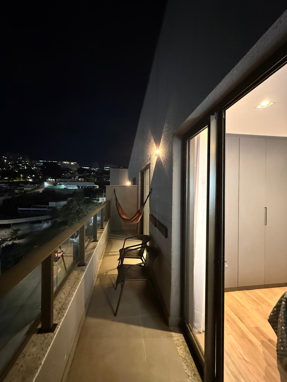 Varanda à noite com rede, poltronas e vista iluminada da cidade